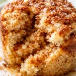 Moist cinnamon mug cake with a swirl of cream cheese frosting and a dusting of cinnamon, served in a mug, displaying a golden-brown crust and gooey center.