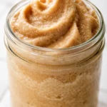 A tall glass of frozen whipped coffee with a creamy, frothy top and a straw, showing rich brown color and smooth texture.
