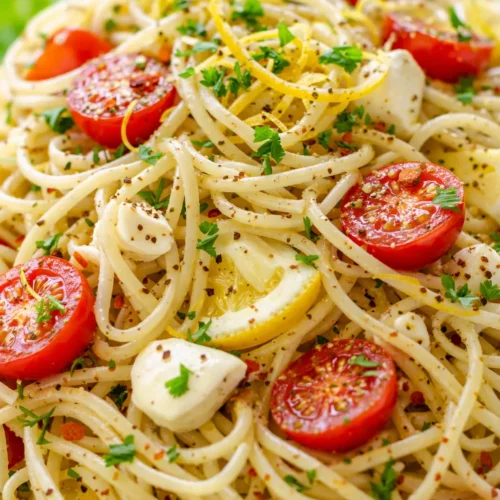 Bright lemon capellini salad with fresh herbs, cherry tomatoes, and glossy pasta strands in a light citrus dressing.