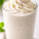 Creamy homemade Starbucks vanilla bean copycat Frappuccino in a tall glass, topped with whipped cream and visible vanilla bean specks.