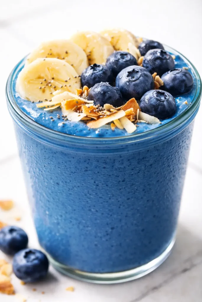 Vibrant blue smoothie bowl topped with fresh berries, sliced banana, granola, and a drizzle of coconut cream, creamy and inviting texture.
