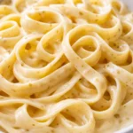 Plated creamy garlic tagliatelle with glossy sauce, fresh parsley, and shaved parmesan on a white plate.