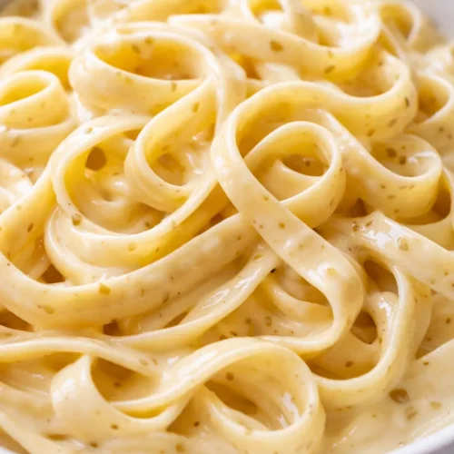 Plated creamy garlic tagliatelle with glossy sauce, fresh parsley, and shaved parmesan on a white plate.
