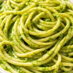 A bowl of creamy green sauce pasta with vibrant spinach-basil sauce, garnished with cherry tomatoes and Parmesan, showcasing its velvety texture.