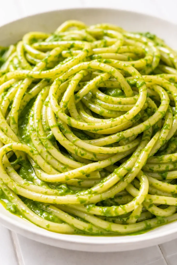 A bowl of creamy green sauce pasta with vibrant spinach-basil sauce, garnished with cherry tomatoes and Parmesan, showcasing its velvety texture.