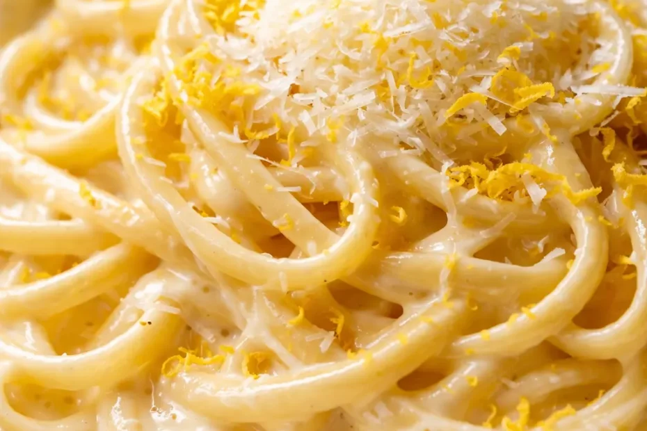 Creamy lemon pasta al dente spaghetti with glossy, pale yellow sauce and fresh parsley flakes on a white plate