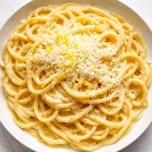 Rich creamy lemon pasta with twirled spaghetti, glossy sauce, and fresh parsley garnish on a white plate.