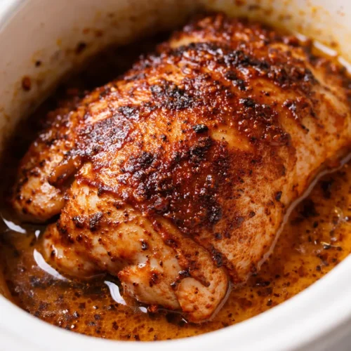 Creamy Crockpot Cajun butter chicken in a white bowl, rich orange sauce with herbs, smooth and creamy texture.