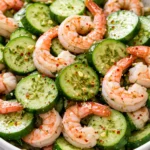 Crisp cucumber slices, plump shrimp, and creamy dressing in a bowl, showcasing a non-soggy salad with vibrant green and pink hues.