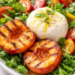 Grilled peach burrata salad with creamy cheese, charred peaches, peppery arugula, and a drizzle of balsamic glaze on a white plate