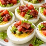 Crisp lettuce, cherry tomatoes, and crispy bacon atop a sliced hard-boiled egg on a white plate, a healthy BLT bite appetizer.