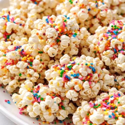 Homemade funfetti marshmallow popcorn treats with rainbow sprinkles on a white platter, crispy and chewy texture.