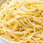 Bright lemon capellini salad with al dente pasta, fresh herbs, and cherry tomatoes in a white bowl, drizzled with tangy dressing.