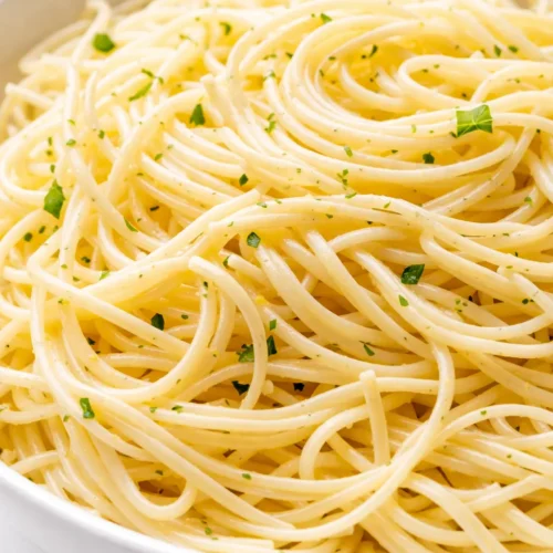 Bright lemon capellini salad with al dente pasta, fresh herbs, and cherry tomatoes in a white bowl, drizzled with tangy dressing.