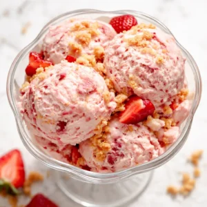 Creamy no-churn strawberry shortcake ice cream in a bowl with swirls of strawberry sauce and pieces of shortcake.