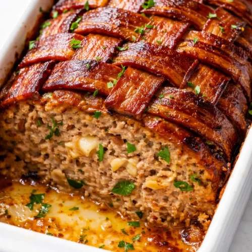 Juicy spicy jalapeño popper meatloaf sliced on a plate with gooey melted cheese and crispy bacon, golden brown crust.