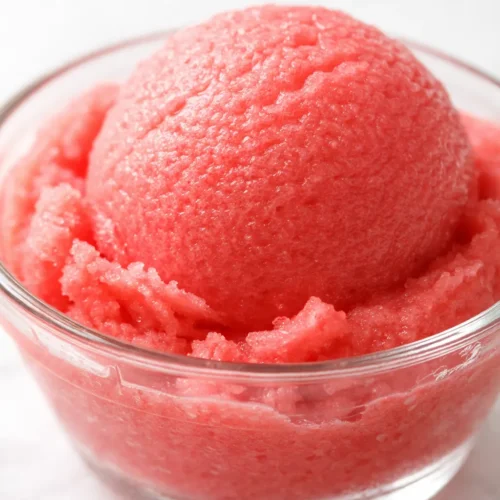 Vibrant pink watermelon sorbet scoop in a white bowl, smooth and icy texture, garnished with fresh mint leaves