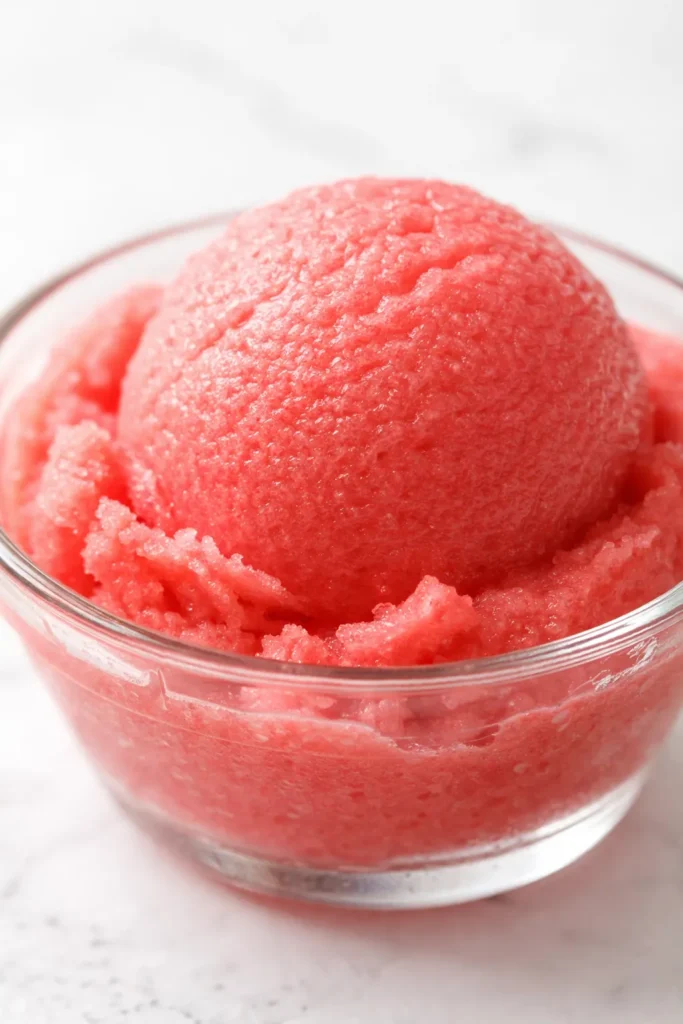 Vibrant pink watermelon sorbet scoop in a white bowl, smooth and icy texture, garnished with fresh mint leaves