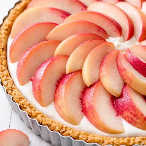 Slice of white peach mascarpone tart on a white plate, revealing creamy filling and golden, flaky crust.