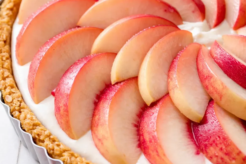 Slice of white peach mascarpone tart on a white plate, revealing creamy filling and golden, flaky crust.
