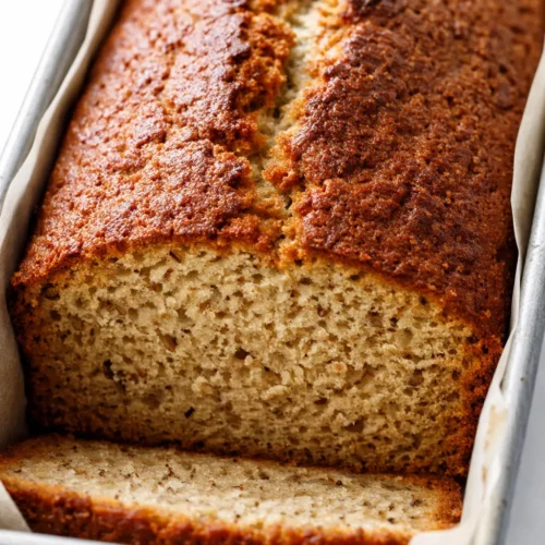 A perfectly moist slice of best banana bread with golden brown crust and tender crumb, showing rich banana color.