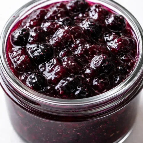 Deep purple blueberry jam with vanilla bean specks in a small jar, thick and glossy texture.