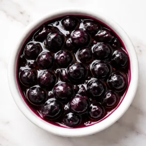 Blueberry sauce simmering on stove with whole berries visible, deep purple color and glossy texture.