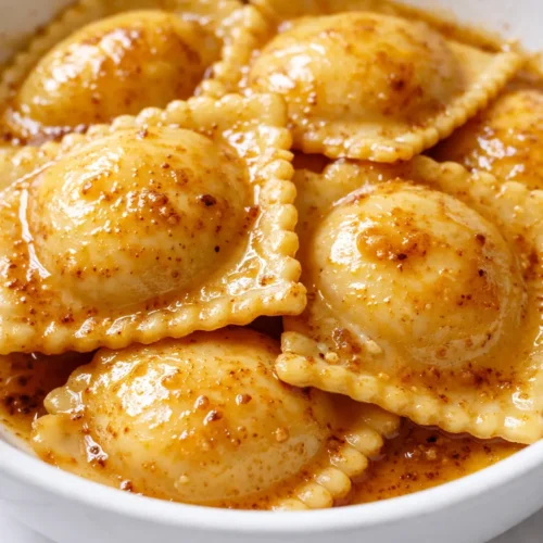 Golden brown butter ravioli sauce coating tender pasta, topped with crispy sage leaves for a glossy, aromatic finish.
