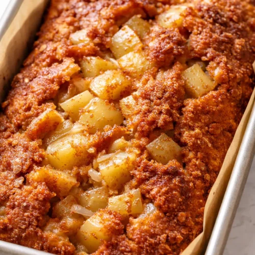 Moist cinnamon apple bread loaf with golden brown crust and cinnamon swirls, sliced to reveal tender apple pieces.