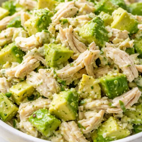 Creamy avocado chicken salad with chunks of ripe avocado, shredded chicken, and a light dressing, garnished with fresh herbs.
