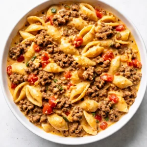 Ground beef browning with diced Rotel tomatoes in a skillet for creamy Rotel pasta, rich red sauce simmering with herbs.