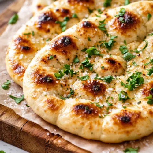 Golden brown garlic naan bread with charred spots and melted butter, soft and fluffy texture on a dark plate.