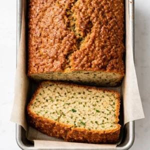 Shredded zucchini folded into thick gluten free batter for moist zucchini bread, with green flecks and smooth texture.