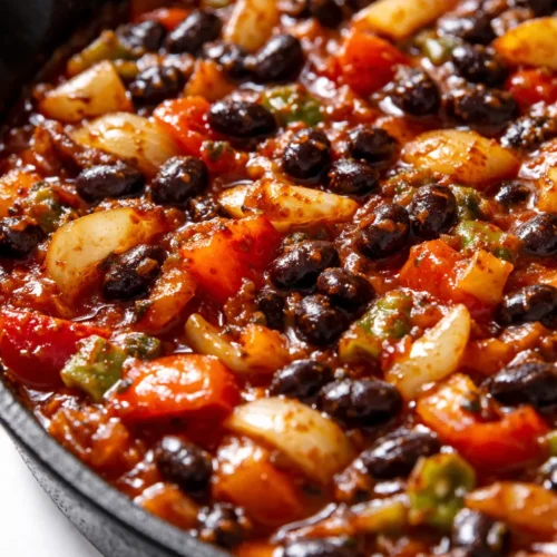 Healthy enchilada skillet with melted cheese, black beans, and fresh cilantro in a cast iron pan, topped with avocado slices.