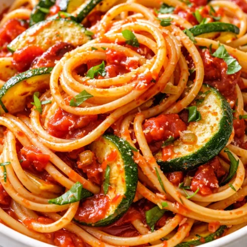Bowl of healthy tomato zucchini pasta with vibrant red sauce, tender zucchini ribbons, and al dente spaghetti, garnished with fresh basil.