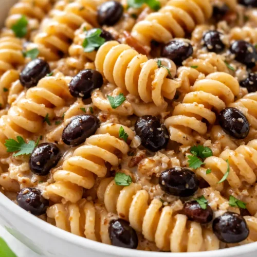 High protein taco pasta with creamy sauce, seasoned ground beef, melted cheese, and taco toppings in a bowl.