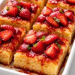 Golden brown shortcake bars layered with juicy strawberries and creamy whipped cream on a white plate.