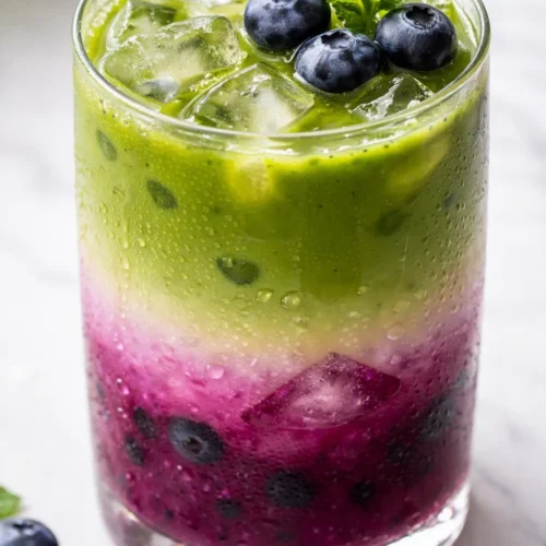 Iced blueberry matcha latte with vibrant green matcha and deep purple blueberry layers, creamy texture over ice.