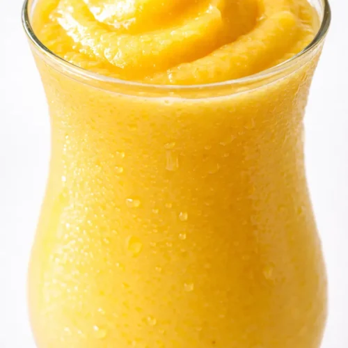 creamy mango colada mocktail in a tall glass, golden yellow color, garnished with coconut and mint