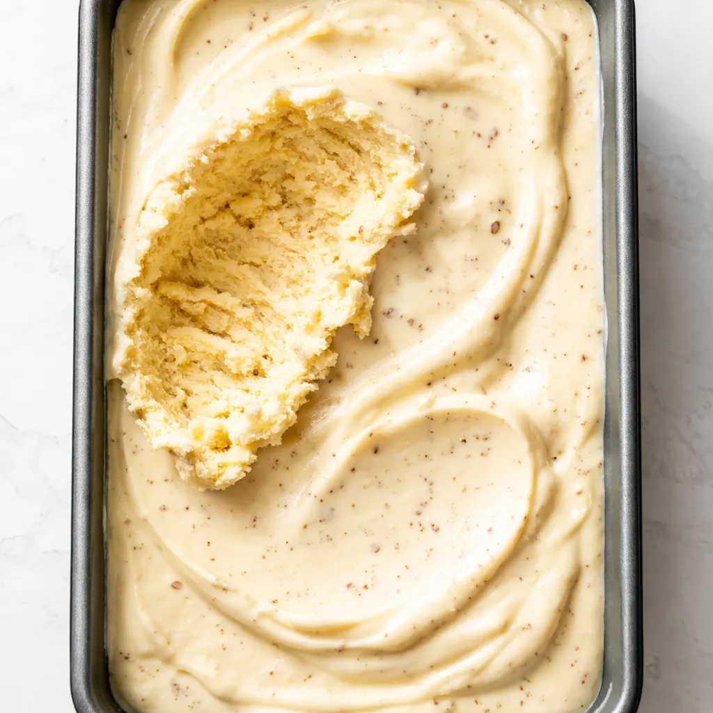 No-churn banana pudding ice cream batter being stirred with vanilla wafers and fresh banana slices, showing a creamy texture.