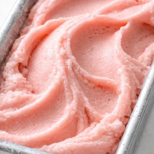 Scoop of creamy no-churn watermelon ice cream in a bowl, vibrant pink with flecks of fruit, smooth texture.