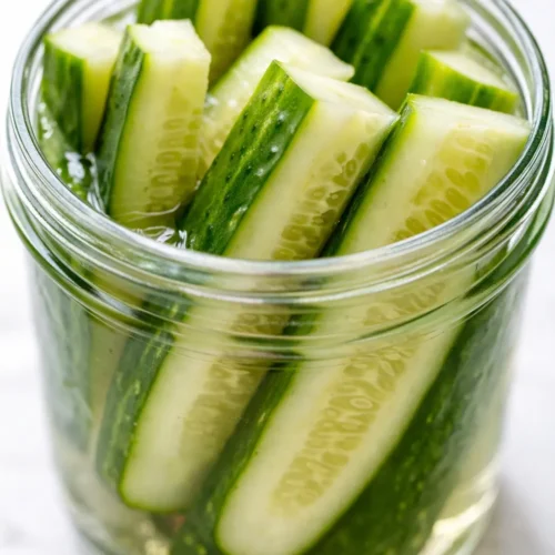Crunchy refrigerator pickles in a mason jar with garlic and dill, bright green cucumbers and golden brine.