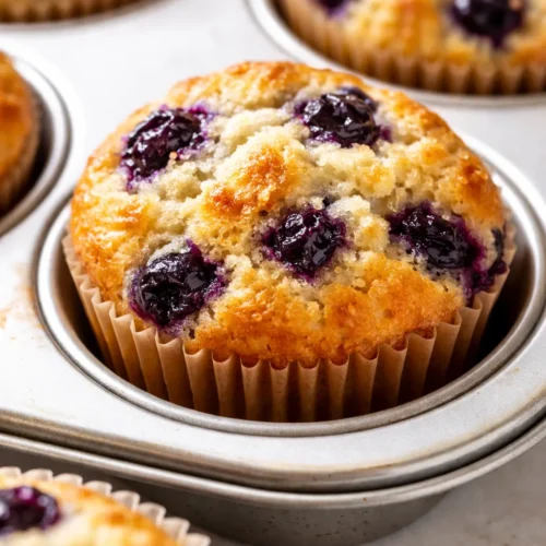 Tall bakery-style blueberry muffins with golden domed tops studded with juicy blueberries, displayed on a rustic wooden board.