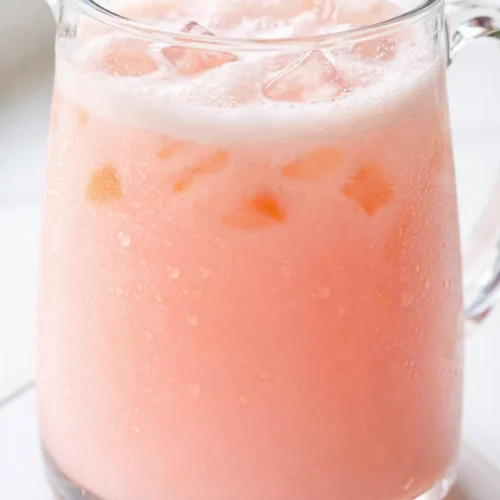 Vibrant pink copycat Starbucks Pink Drink in a tall glass with ice, strawberries, and a creamy coconut milk swirl.