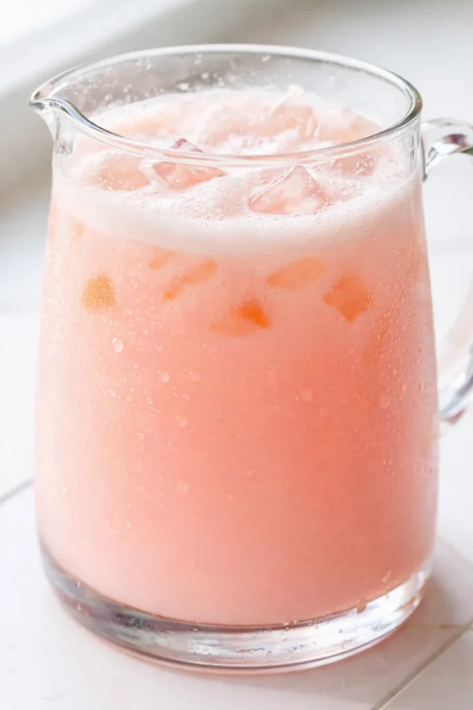 Vibrant pink copycat Starbucks Pink Drink in a tall glass with ice, strawberries, and a creamy coconut milk swirl.