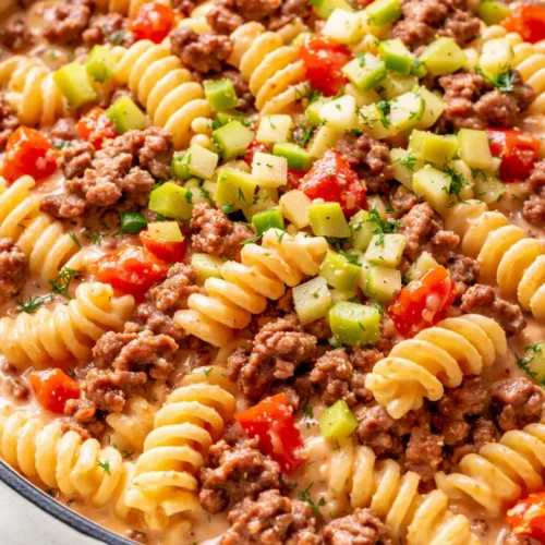 Creamy cheeseburger pasta with ground beef, melted cheddar, and pickles in a cast iron skillet, ready in 30 minutes.