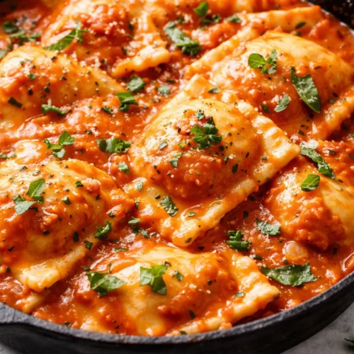 Creamy tomato ravioli sauce coating cheese ravioli, garnished with basil and parmesan, rich red-orange color.