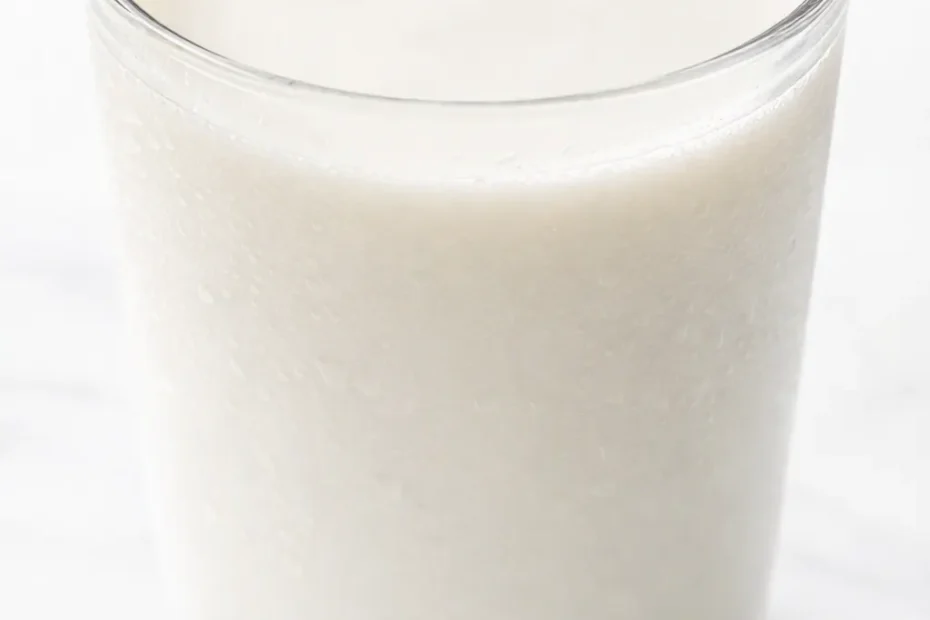 Creamy homemade almond milk in a glass pitcher, pale ivory and velvety, with whole almonds and a cinnamon stick beside it.