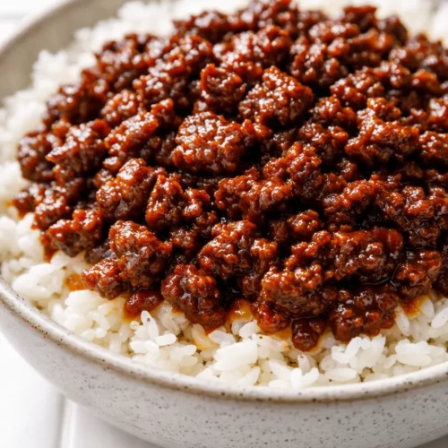 Korean ground beef bowl with steamed rice, sauteed vegetables, and a glossy soy-sesame glaze garnished with green onions and sesame seeds.