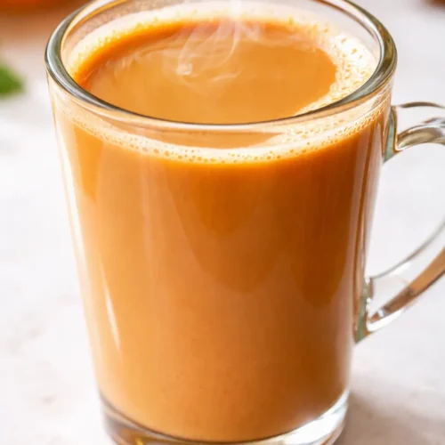 Creamy orange cinnamon milk tea in a glass mug, warm orange tones with a cinnamon stick and dried orange slice, smooth and inviting.
